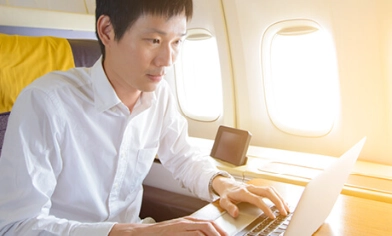 Man on plane in upgraded seating working on his laptop