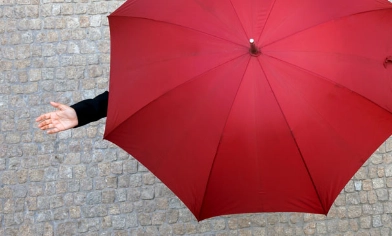 Person on cobble street under an open red umbrella holding their hand out to feel the rain